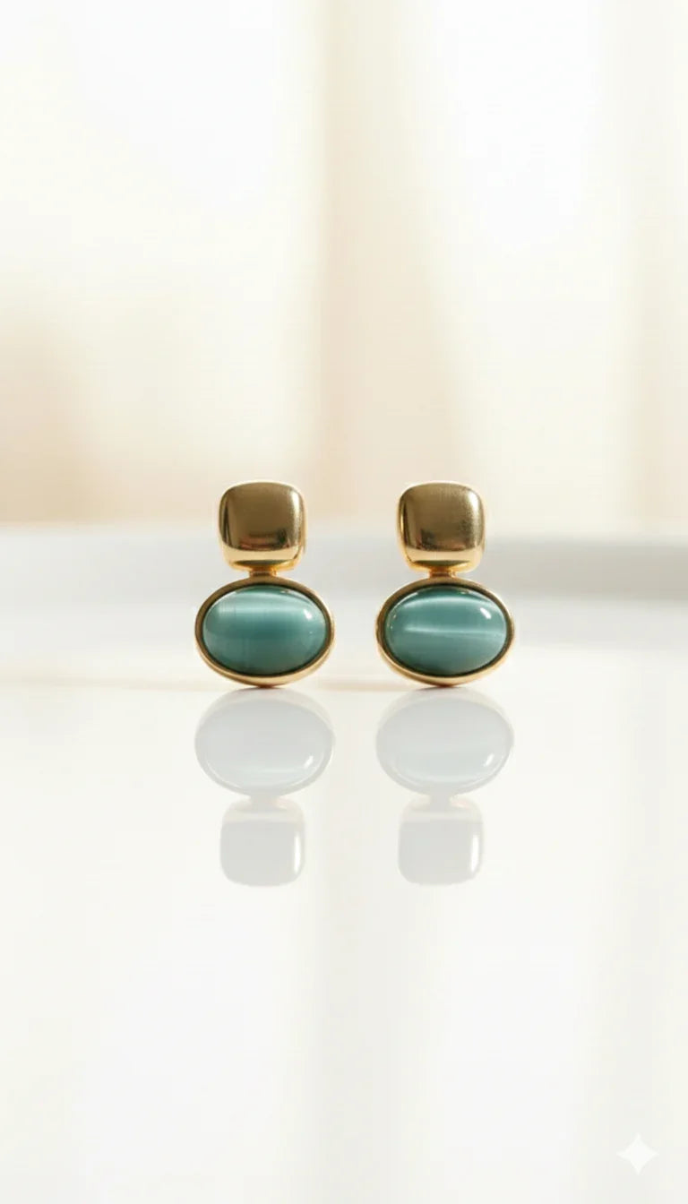 Orecchini dorati con pietra ovale verde acqua su sfondo chiaro, eleganti e luminosi.