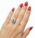 Anello elegante con pietra blu rettangolare e contorno di piccoli diamanti su mano femminile