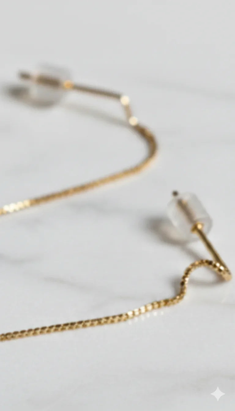 Orecchini sottili a catena dorata con chiusura in silicone su sfondo marmo, gioielli eleganti
