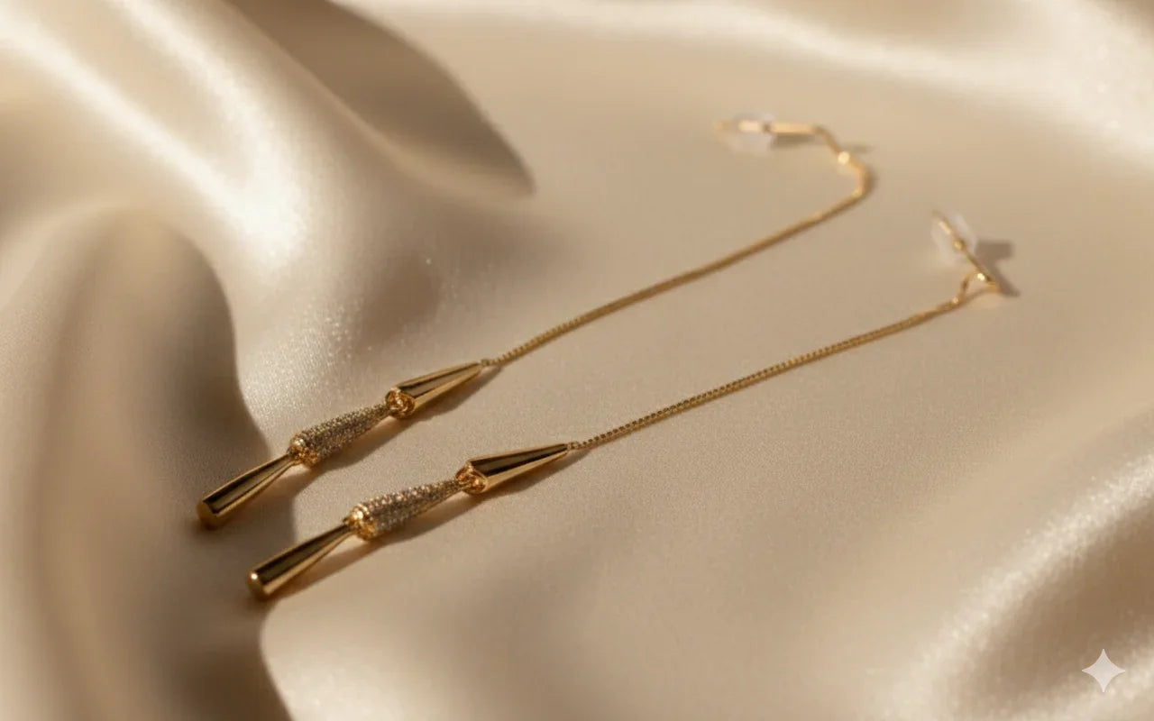 Orecchini pendenti oro lunghi su tessuto beige, design elegante e raffinato