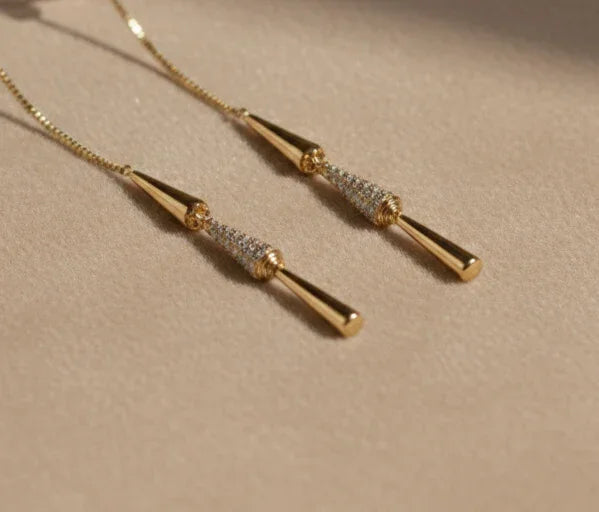 Orecchini pendenti dorati con dettagli brillanti su sfondo beige elegante