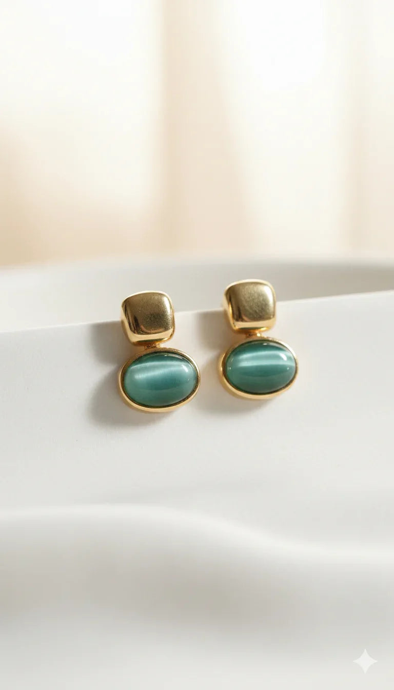 Orecchini dorati con pietra verde ovale, design elegante e raffinato su sfondo chiaro.