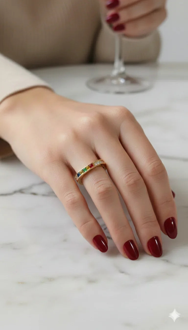 Mano femminile con un anello oro con pietre colorate su sfondo di marmo, unghie rosse eleganti